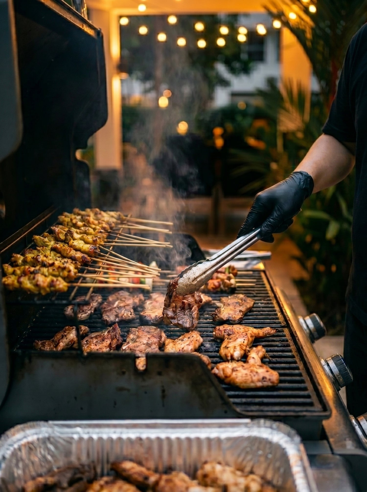Professional BBQ chef for hire grilling chicken, satay skewers, and beef at an 
outdoor private event in Singapore
